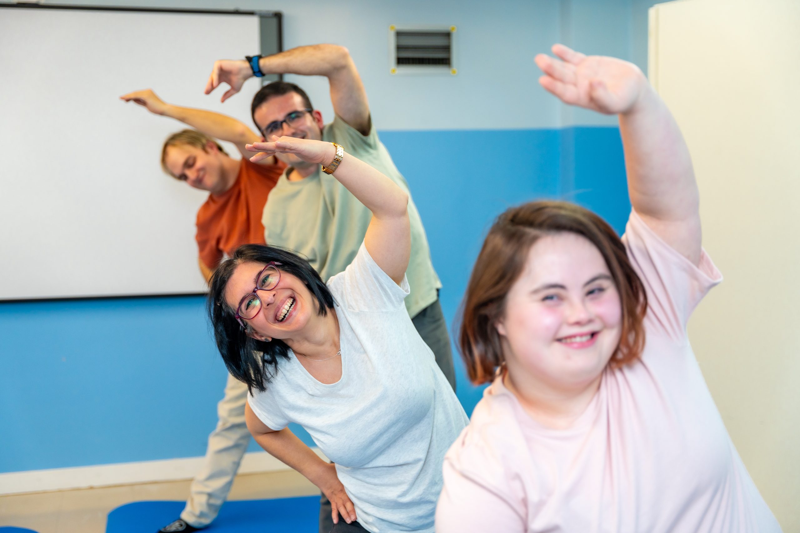 In a brightly lit room, a diverse group of four individuals is joyfully doing a side stretch on exercise mats, their smiles radiating positive energy. #SamplePost1.